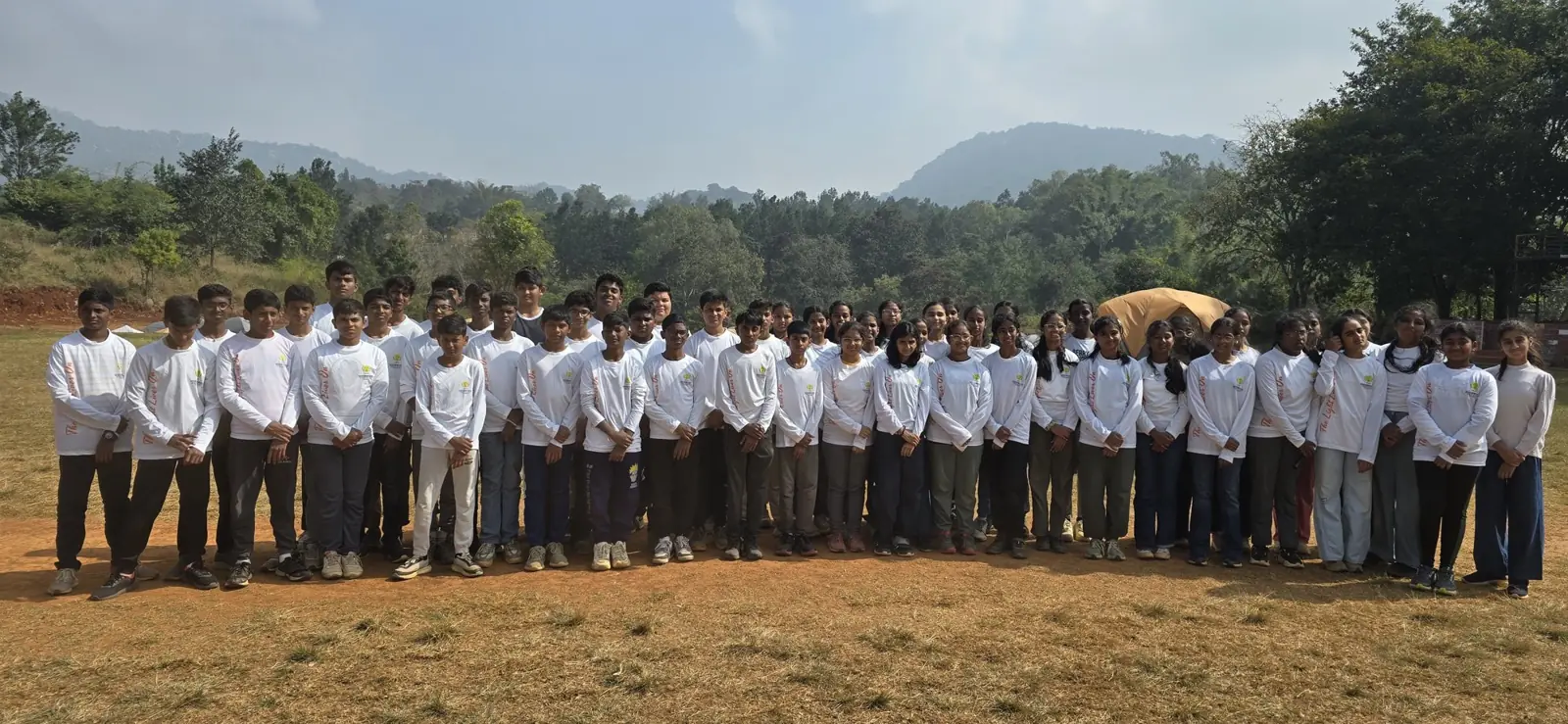 A school group in white shirts at a valley campsite