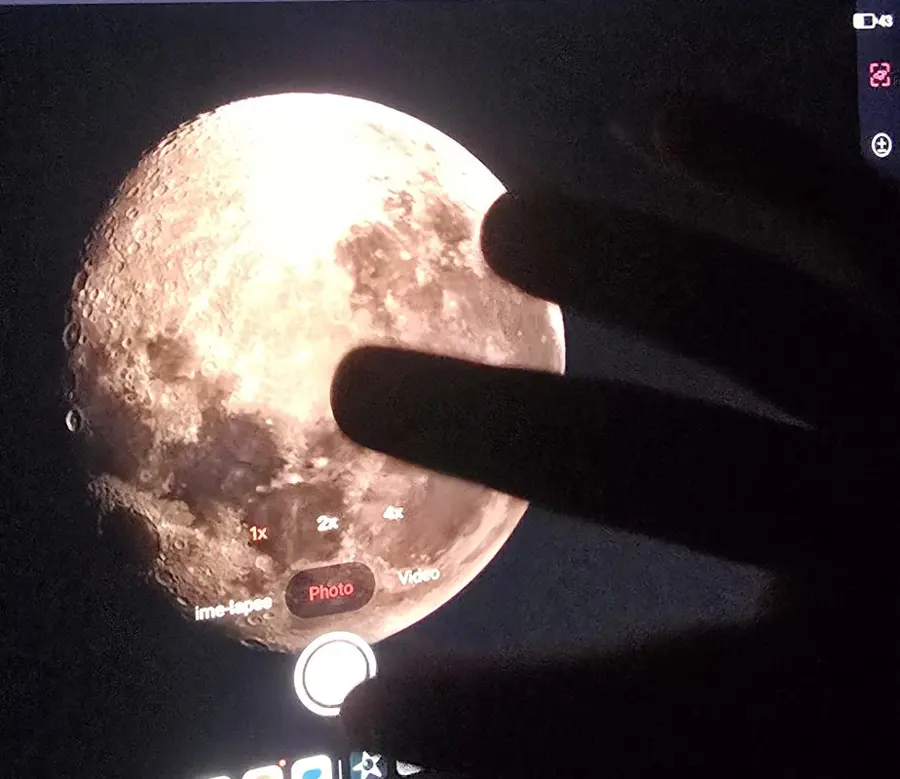 The moon shown live on a tablet connected to a telescope, with students pointing