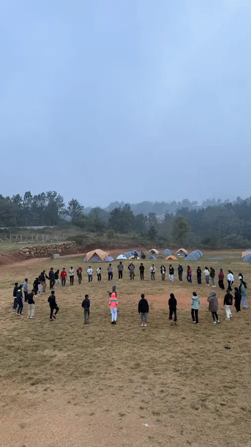 Students standing in a large circle on the campsite field at dawn
