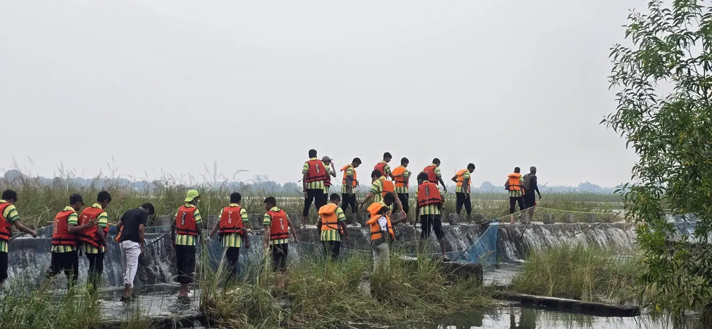 Students in life jackets wading across a shallow weir